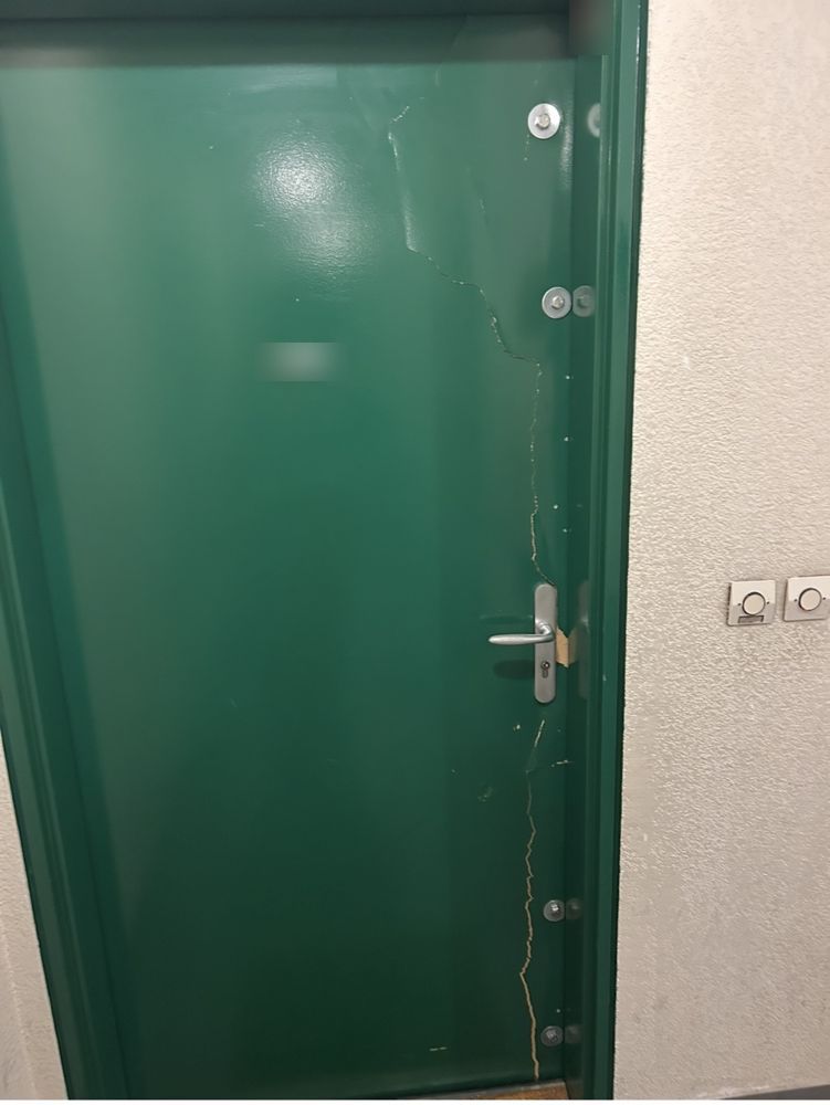 Porte verte fissurée et déformée après une effraction, avant son remplacement